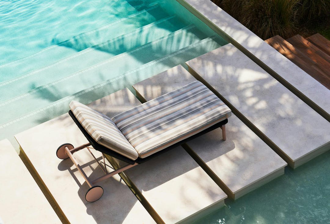 Ann Marie Vering's Oscar collection of a chaise lounge with wheels in the middle of a contemporary pathway surrounded by a pool. Light soft pattern fabrics and pink finish.