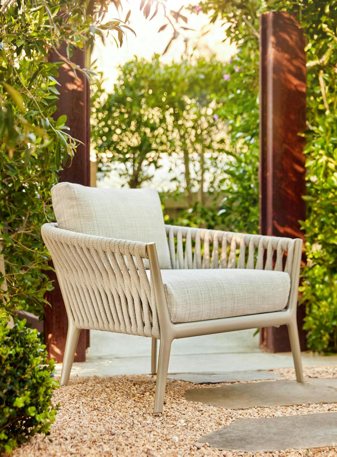 Lounge chair with white fabric and finish cropped close with 2 red poles and greenery behind. H Lounge was designed by Toan Nguyen.